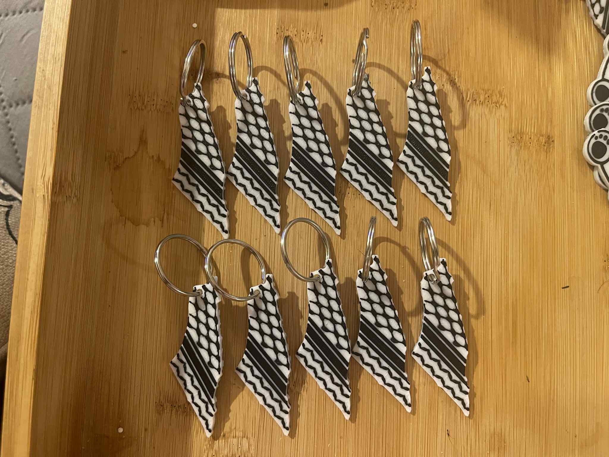 “Kuffiyeh pattern keychains packaged with thank you tags on wooden surface.”
“Set of Palestinian-inspired black and white woven fabric keyrings.”
“Cultural kuffiyeh keychain with metal loop symbolizing solidarity and heritage.”